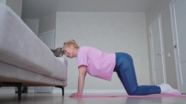 Bir kadın evde yoga yapıyor, kedisiyle bağ kuruyor. Kedi eşliğinde rahat bir antrenman.