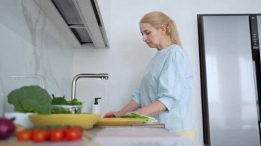 Modern bir mutfakta, bir kadın taze ve renkli malzemeler kullanarak sağlıklı bir yemek pişirmek için canlı sebzeler yıkıyor.