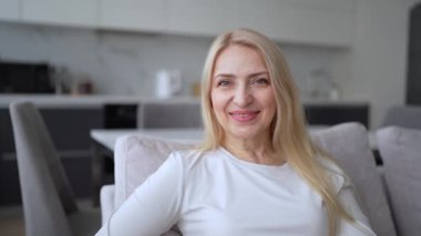 Neşeli bir kadın modern evindeki bir kanepede rahatça oturuyor, rahat ve mutlu görünüyor..