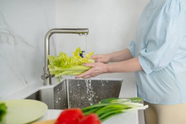 Modern bir mutfakta, bir kadın taze ve renkli malzemeler kullanarak sağlıklı bir yemek pişirmek için canlı sebzeler yıkıyor.