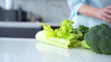 Bir kadın, yeniden kullanılabilir bir çantadaki taze sebzeleri modern bir mutfaktan çıkarır ve çevre dostu alışkanlıkları teşvik eder..