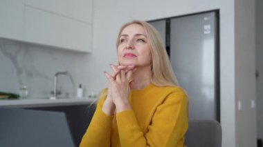 Sarışın bir kadın profesyonel dizüstü bilgisayar üzerinde çalışıyor ve doğal ışık alan rahat bir ofis ortamında notlar alıyor.