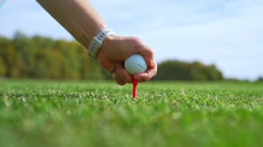 Bir golfçü golf topunu dikkatlice bir golf topuna yerleştiriyor, tamamen hazır ve güneşli bir günde mükemmel atış için hazır.