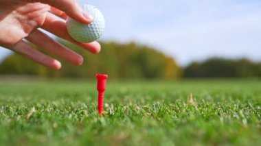 Bir golfçü golf topunu dikkatlice bir golf topuna yerleştiriyor, tamamen hazır ve güneşli bir günde mükemmel atış için hazır.