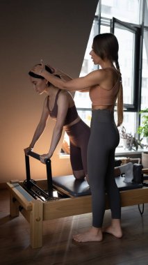 Pilates eğitmeni stüdyoda pilates makinesinde çalışıyor. Pilates hocası bir öğrenciye egzersiz dersinde yardım ediyor..