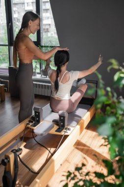 Bir pilates eğitmeni öğrenciye egzersizlerde rehberlik eder, teknik ve genel refah üzerine yoğunlaşır.