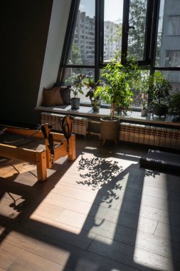 Pilates reformcusu ve Dengeli Vücut Merdiveni Fıçısı ekipmanı büyük pencerelerden gelen doğal ışıkla çağdaş bir fitness stüdyosunda..