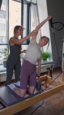 Yetenekli bir pilates eğitmeni, müşteriyi yatıştırıcı bir stüdyoda esneme egzersizinde dikkatlice yönlendirir.