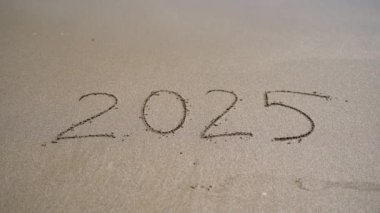 2025 yılı, güzel bir şekilde sıcak kuma oyulmuş, gelecekteki arzularımızı ve gelecek anlamlı anları simgeliyor.