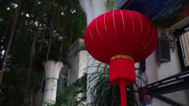 Sanya, Çin - 9 Ekim 2024: Zarif altın aksanıyla süslenmiş güzel bir kırmızı fener, yemyeşil bir arka plana karşı kurulmuştur.