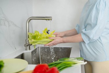 Modern bir mutfakta, bir kadın taze ve renkli malzemeler kullanarak sağlıklı bir yemek pişirmek için canlı sebzeler yıkıyor.