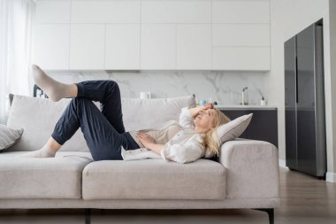 Zarif bir kadın modern dekorlu ve doğal ışıklandırmalı modern bir oturma odasında şık bir koltukta dinleniyor.