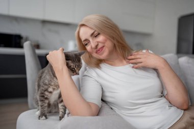 Neşeli bir kadın modern evindeki bir kanepede rahatça oturuyor, rahat ve mutlu görünüyor..