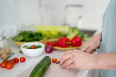 Modern bir mutfakta, bir kadın taze sebzelerin arasında salatalık keserek sağlıklı bir yemek hazırlıyor.
