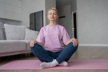 Son sınıf öğrencisi kadın bağdaş kurup yoga minderinde meditasyon yapıyor. Sakinlik ve rahatlığı kucaklıyor..