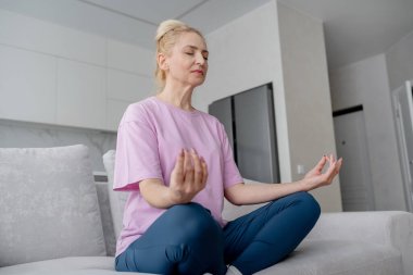 Son sınıf öğrencisi kadın bağdaş kurup yoga minderinde meditasyon yapıyor. Sakinlik ve rahatlığı kucaklıyor..