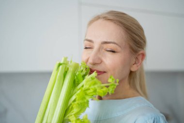Genç bir kadın, modern bir mutfakta taze kereviz yiyor. Sağlıklı bir yaşam tarzına bağlılığını gösteriyor.