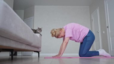 Bir kadın evde yoga yapıyor, kedisiyle bağ kuruyor. Kedi eşliğinde rahat bir antrenman.
