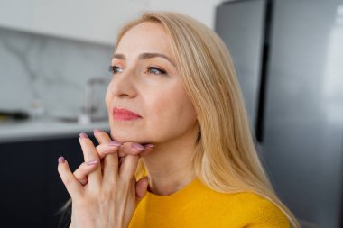Sarışın bir kadın profesyonel dizüstü bilgisayar üzerinde çalışıyor ve doğal ışık alan rahat bir ofis ortamında notlar alıyor.