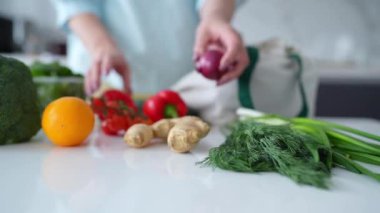 Bir kadın, yeniden kullanılabilir bir çantadaki taze sebzeleri modern bir mutfaktan çıkarır ve çevre dostu alışkanlıkları teşvik eder..