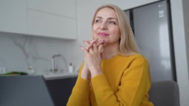 Sarışın bir kadın profesyonel dizüstü bilgisayar üzerinde çalışıyor ve doğal ışık alan rahat bir ofis ortamında notlar alıyor.