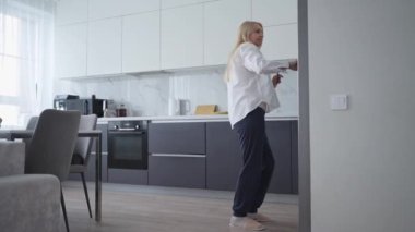 Parlak, modern bir mutfakta, sarışın bir kadın beyaz dolaplar arasında yemek pişirir, şık ve temiz bir ortam yaratır.