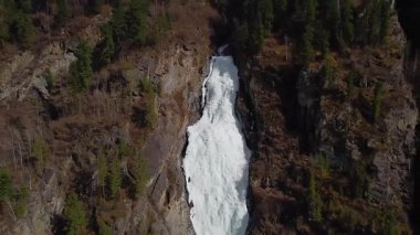 Çam ormanlarıyla çevrili kayalık uçurumlardan dökülen donmuş bir şelalenin çarpıcı hava manzarası..