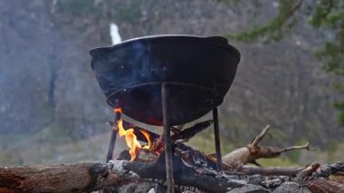 Sağlam bir dökme demir tencere kamp ateşinin üzerinde oturur, çarpıcı doğayla çevrili, açık hava yemekleri için mükemmeldir.