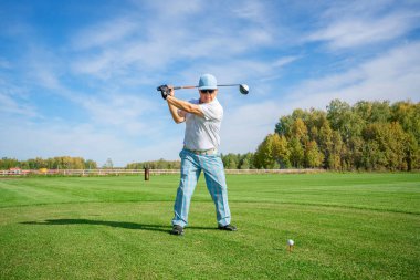 Yetenekli bir golfçü, açık mavi gökyüzünün altında güçlü bir vuruş yapar.