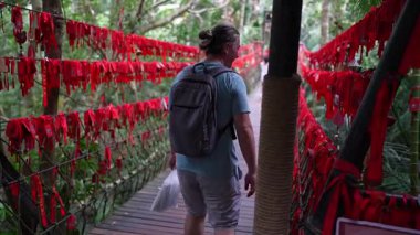 Yalong Körfezi, Çin - 14 Ekim 2024: Bereketli tropikal cennet ormanı parkı ile çevrili kırmızı kurdeleli canlı bir aşk köprüsü