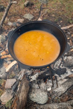 Canlı ve renkli bir tencere lezzetli yiyecek güzel doğal bir manzarada açık bir kamp ateşinin üzerinde kaynıyor.