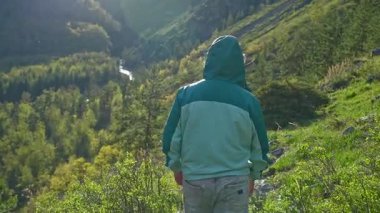 Rahat bir kapüşonlu giyen biri çarpıcı, canlı yeşil bir manzaranın içinde duruyor, güzelliğin tadını çıkarıyor.