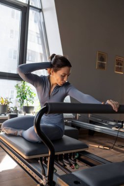 Güneş ışığı, modern pilates stüdyosunda deniz kızı egzersizi yapan kadın sakin, odaklanmış ve güçlü.