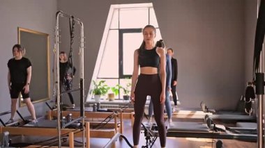 Genç beyaz kadınlar parlak bir stüdyoda pilates reformcuları üzerinde egzersiz yapıyorlar. Onların çalışmaları modern bir fitness ortamında çekirdek kuvveti ve esnekliği üzerine odaklanır..