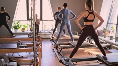 Genç beyaz kadınlar parlak bir stüdyoda pilates reformcuları üzerinde egzersiz yapıyorlar. Onların çalışmaları modern bir fitness ortamında çekirdek kuvveti ve esnekliği üzerine odaklanır..
