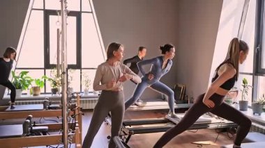 Genç beyaz kadınlar parlak bir stüdyoda pilates reformcuları üzerinde egzersiz yapıyorlar. Onların çalışmaları modern bir fitness ortamında çekirdek kuvveti ve esnekliği üzerine odaklanır..