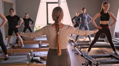 Genç beyaz kadınlar parlak bir stüdyoda pilates reformcuları üzerinde egzersiz yapıyorlar. Onların çalışmaları modern bir fitness ortamında çekirdek kuvveti ve esnekliği üzerine odaklanır..