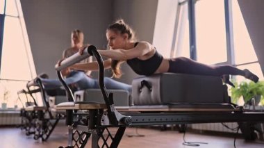 Kuğu egzersizi yapan kadınlar, göğüs ve sırt kasları için Pilates Reformcusu, esneklik, güç ve kararlılıkla kontrol üzerine odaklanıyorlar.