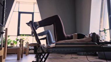 Bir grup kadın, kalça ve pelvise odaklanan, güneş ışığı altında reformist bir yatak makinesinde Glute Köprüsü 'nü çalıştırıyor.