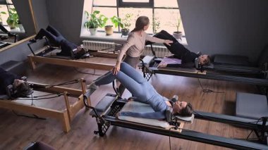 Bir grup kadın, kalça ve pelvise odaklanan, güneş ışığı altında reformist bir yatak makinesinde Glute Köprüsü 'nü çalıştırıyor.