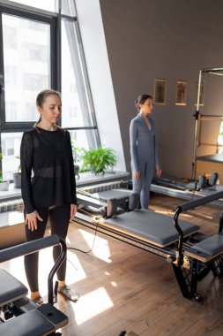 Genç beyaz kadın pilates salonunun parlak stüdyosunda egzersiz yapıyor. Onların çalışmaları modern bir fitness ortamında çekirdek kuvveti ve esnekliği üzerine odaklanır.