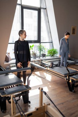 Genç beyaz kadın pilates salonunun parlak stüdyosunda egzersiz yapıyor. Onların çalışmaları modern bir fitness ortamında çekirdek kuvveti ve esnekliği üzerine odaklanır.