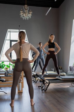 Genç beyaz kadınlar parlak bir stüdyoda pilates reformcuları üzerinde egzersiz yapıyorlar. Onların çalışmaları modern bir fitness ortamında çekirdek kuvveti ve esnekliği üzerine odaklanır..