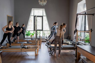 Genç beyaz kadınlar parlak bir stüdyoda pilates reformcuları üzerinde egzersiz yapıyorlar. Onların çalışmaları modern bir fitness ortamında çekirdek kuvveti ve esnekliği üzerine odaklanır..