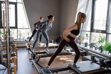 Genç beyaz kadınlar parlak bir stüdyoda pilates reformcuları üzerinde egzersiz yapıyorlar. Onların çalışmaları modern bir fitness ortamında çekirdek kuvveti ve esnekliği üzerine odaklanır..