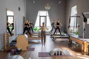 Genç beyaz kadınlar parlak bir stüdyoda pilates reformcuları üzerinde egzersiz yapıyorlar. Onların çalışmaları modern bir fitness ortamında çekirdek kuvveti ve esnekliği üzerine odaklanır..
