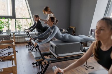 Kuğu egzersizi yapan kadınlar, göğüs ve sırt kasları için Pilates Reformcusu, esneklik, güç ve kararlılıkla kontrol üzerine odaklanıyorlar.