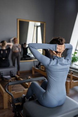 Kadın, göğüs ve sırt kasları için Pilates Reformcusu üzerinde rotasyon egzersizi yapıyor. Kararlılıkla esneklik, güç ve kontrole odaklanıyor..