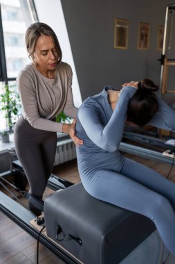 Kadın, göğüs ve sırt kasları için Pilates Reformcusu üzerinde rotasyon egzersizi yapıyor. Kararlılıkla esneklik, güç ve kontrole odaklanıyor..