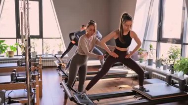 Genç beyaz kadınlar parlak bir stüdyoda pilates reformcuları üzerinde egzersiz yapıyorlar. Onların çalışmaları modern bir fitness ortamında çekirdek kuvveti ve esnekliği üzerine odaklanır..